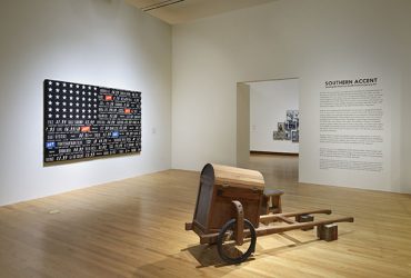 Gallery installation view, with a work in the foreground by Theaster Gates, Soul Food Rickshaw for Collard Greens and Whiskey, 2012/2016. In the background, on the left: Skylar Fein's Black Flag (For Elizabeth’s). Photo by Peter Paul Geoffrion.