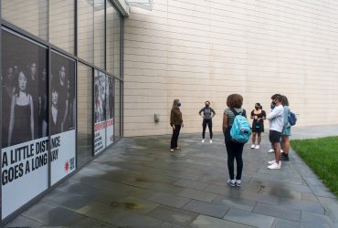 Gallery Guide Ruth Caccavale (far left) leads Duke students in a tour of RESIST COVID / TAKE 6! The window clings behind the students were created by artist Carrie Mae Weems and Social Studies 101 in association with Pierre Loving and THE OFFICE performing arts + film. Photo by J Caldwell.