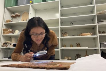 Diana Sanchez demonstrates how to use a magnifying glass with a light to view details in an ancient textile