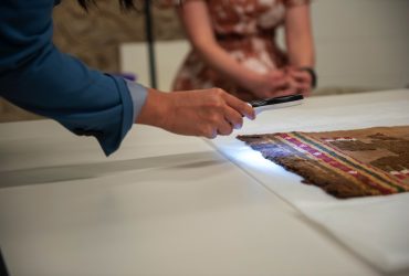 Museum staff use a magnifying glass with a light to view details in ancient works of art