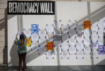 A Duke student adds a poster to the Democracy Wall at the Nasher Museum