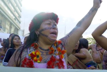 Amazonia: The New Minamata? (film still) Protestor raises fist to the air in a crowd of fellow activists